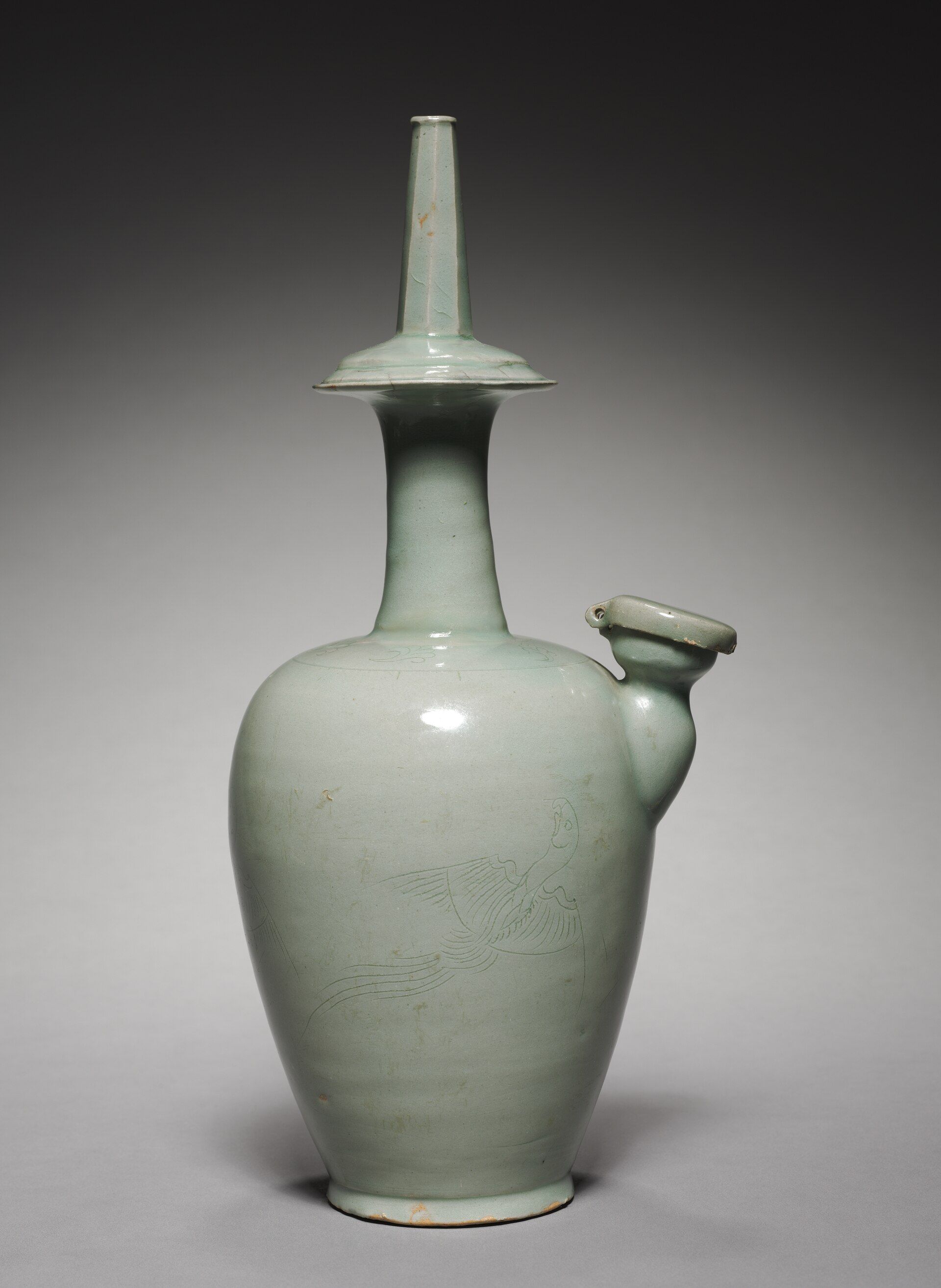 Antigua jarra de agua ritual (kundika) con intrincado diseño de loro, símbolo de purificación.