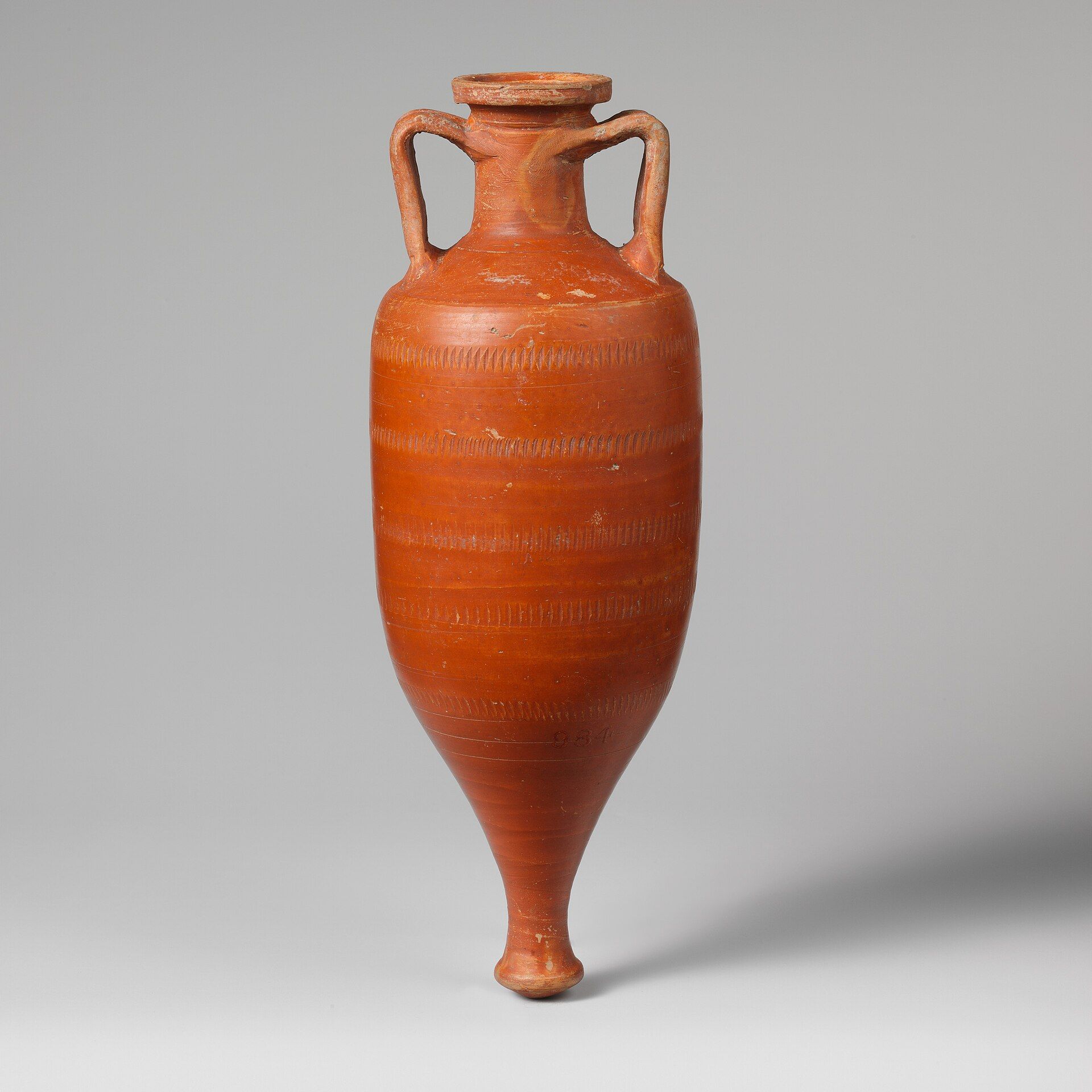 Una ánfora de terracota de color naranja rojizo con dos asas y base puntiaguda sobre fondo gris.