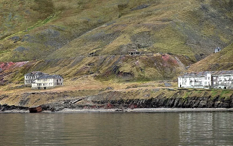 Asentamiento abandonado de Grumant en Svalbard, con edificios ruinosos junto a la orilla y colinas áridas.