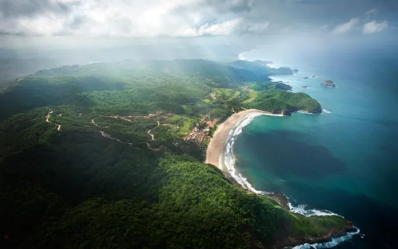 Vista aérea de la playa curvada de Costa Esmeralda, rodeada de selva verde, acantilados y aguas turquesas bajo nubes
