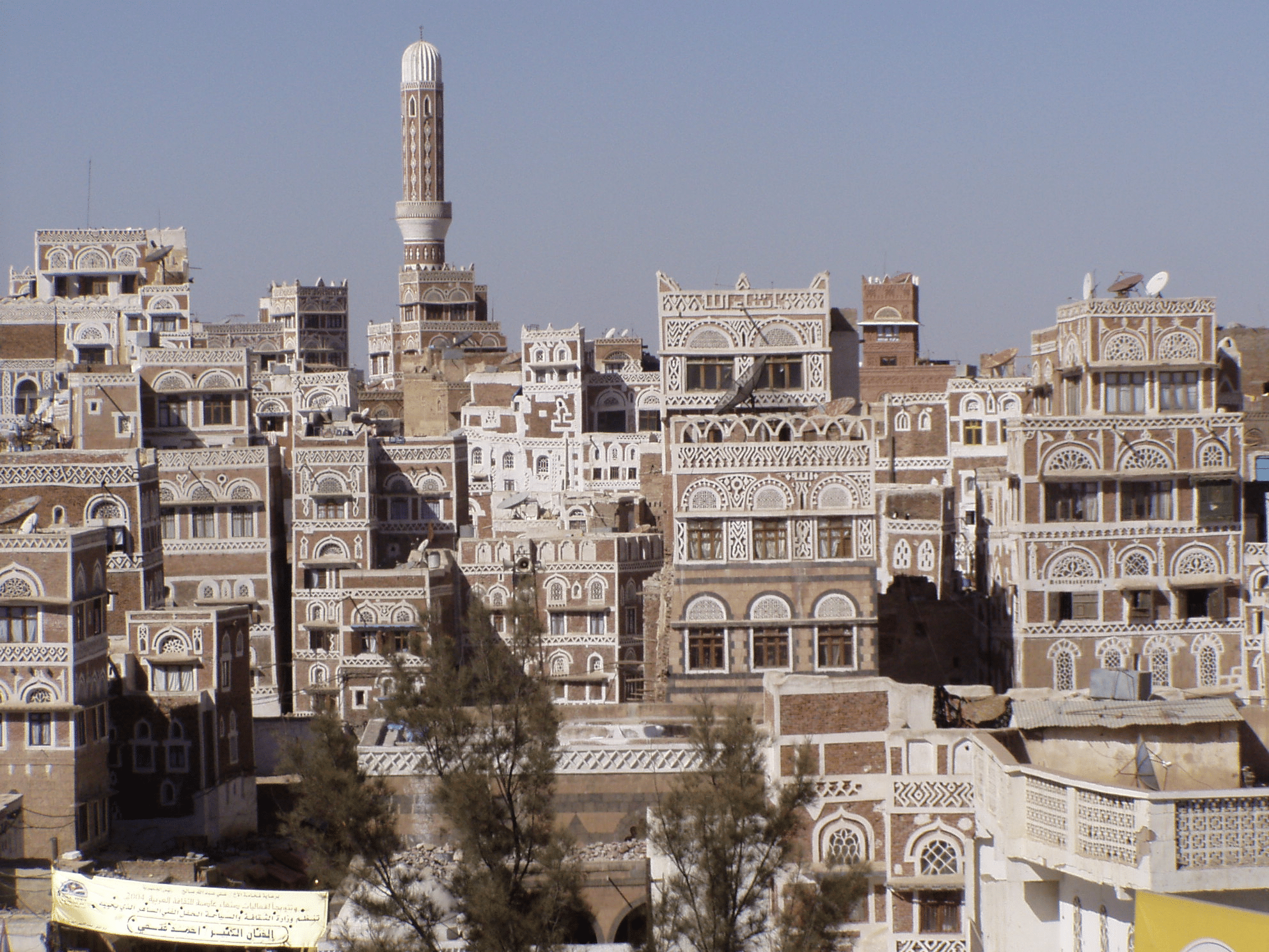 Vista panorámica de Sana'a en Yemen, con casas tradicionales de adobe apiladas, minarete alto y cielo azul claro