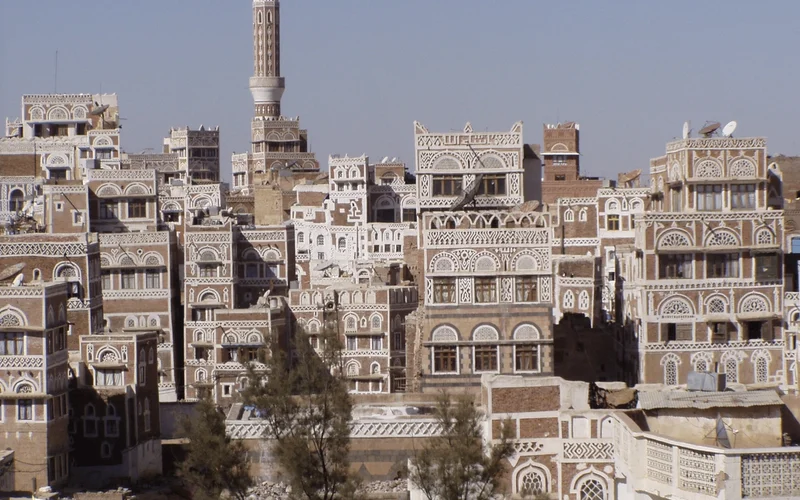 Vista panorámica de Sana'a en Yemen, con casas tradicionales de adobe apiladas, minarete alto y cielo azul claro