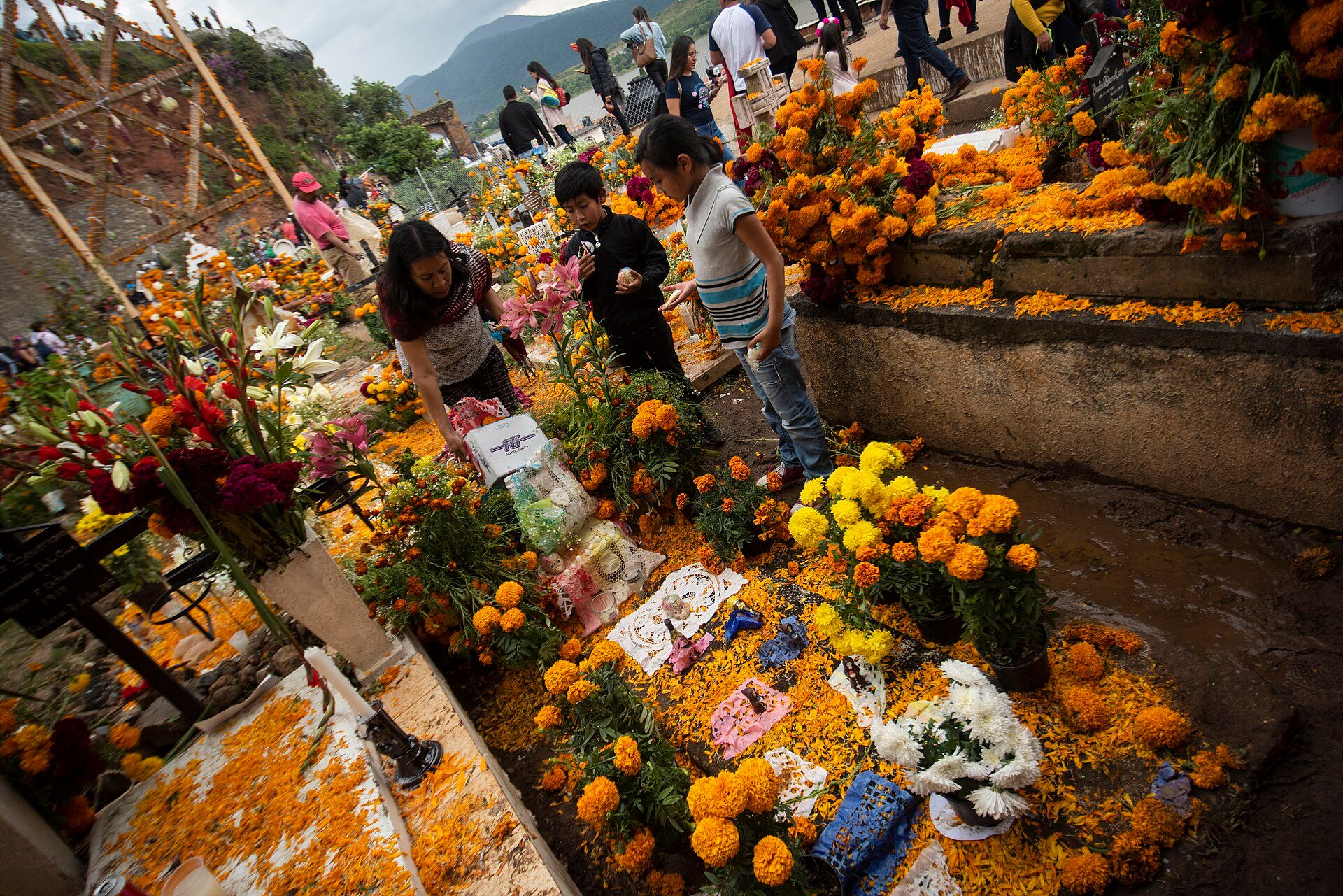 Familia decora una tumba con flores de cempasúchil y velas en un panteón de Michoacán.