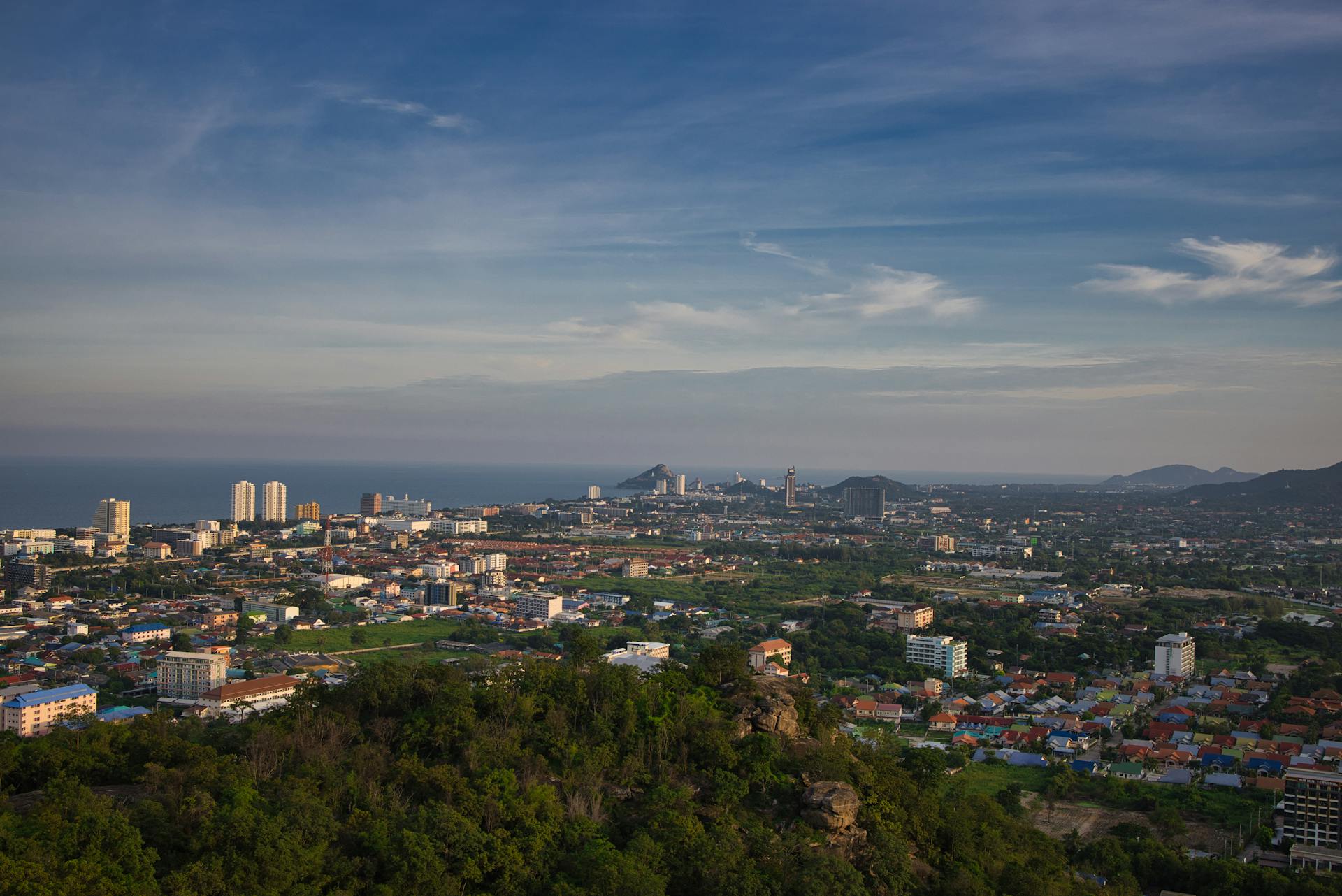 Vista panorámica de Hua Hin con rascacielos junto al mar, colinas verdes y cielo azul al atardecer