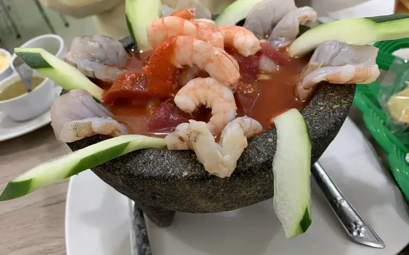 Plato de aguachile en molcajete de piedra negra con camarones rosados, rodajas de pepino, cebolla roja y caldo tomate