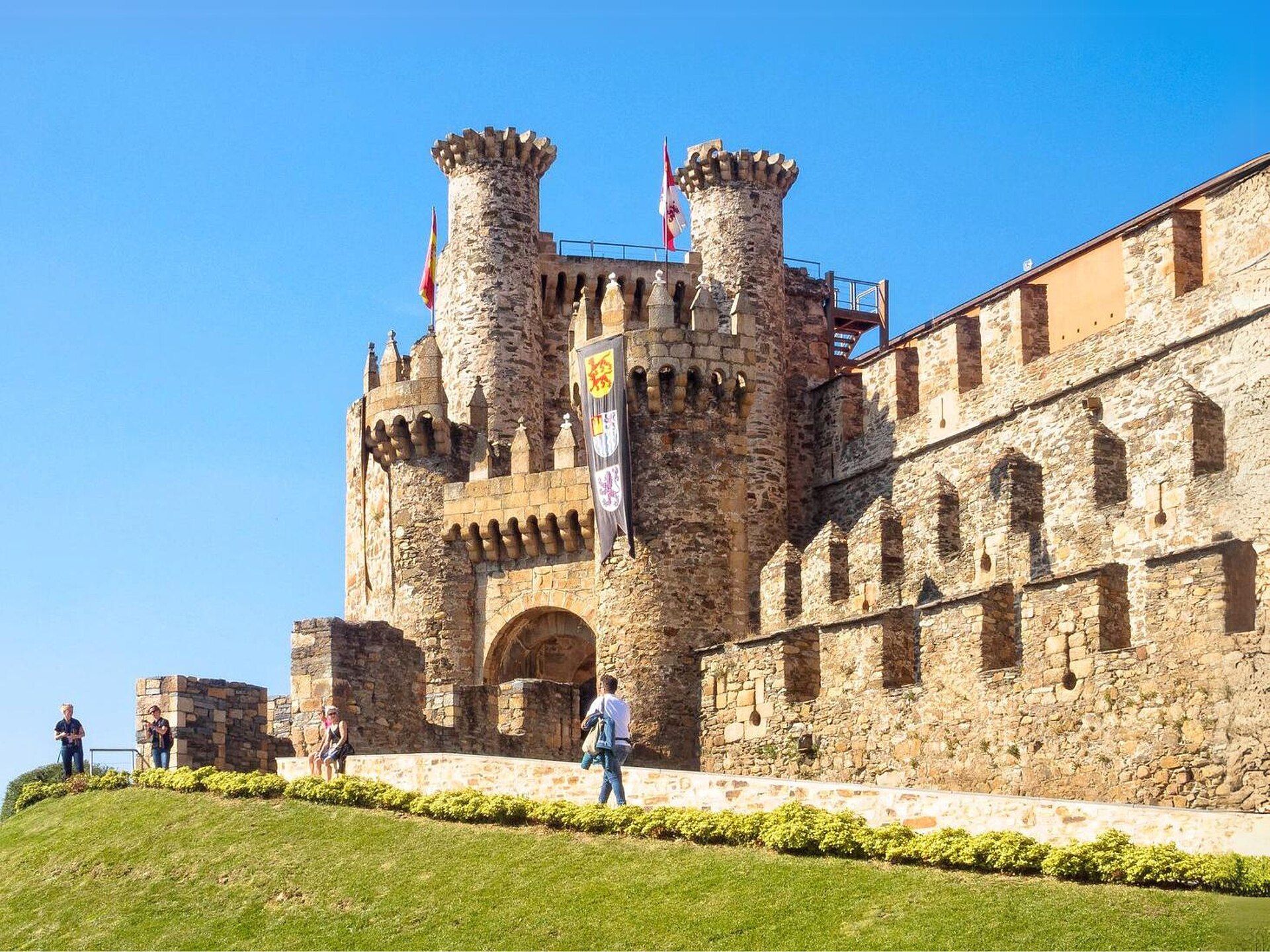 Vista exterior del Castillo de los Templarios de Ponferrada con cielo azul y césped verde.