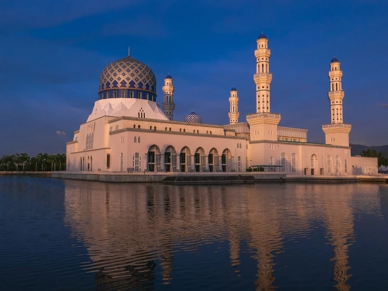 Mezquita con cúpula azul y minaretes blancos reflejada en un lago al atardecer en Kota Kinabalu