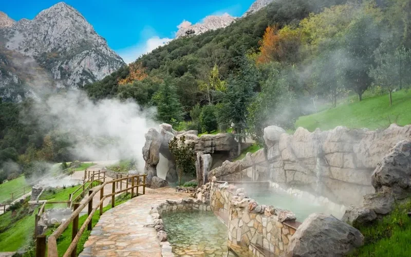 Piscinas termales al aire libre en Balneario de la Hermida, con vapor ascendiendo entre rocas y vegetación montañosa otoñal