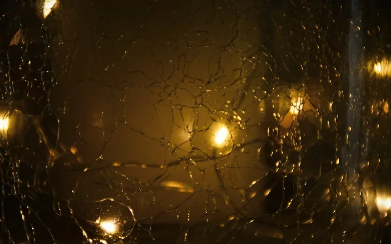 Superficie de vidrio agrietado en tonos dorados con reflejos de luces brillantes