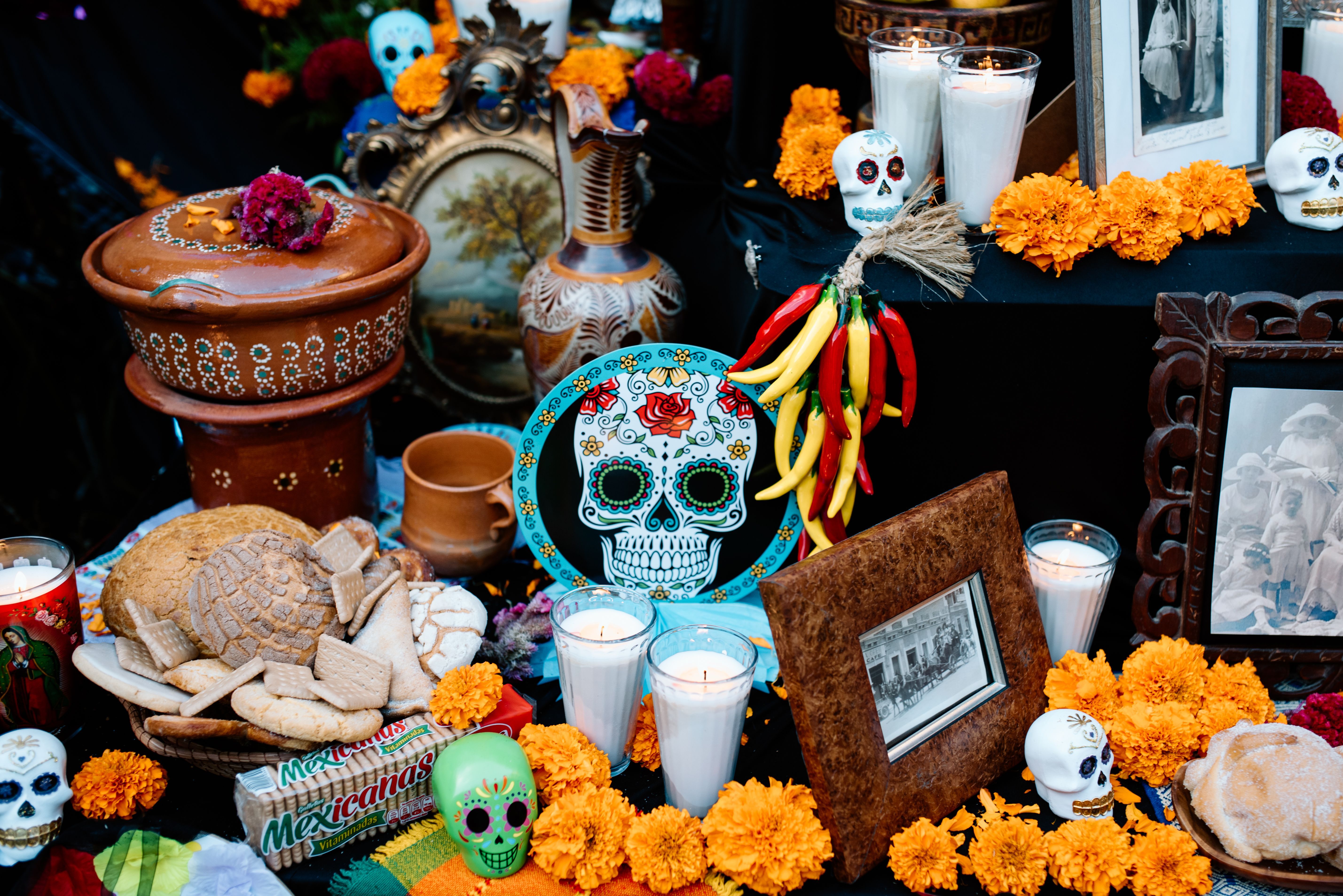 Un altar de Día de Muertos con calaveras de azúcar, pan de muerto, velas, cempasúchil y chiles.