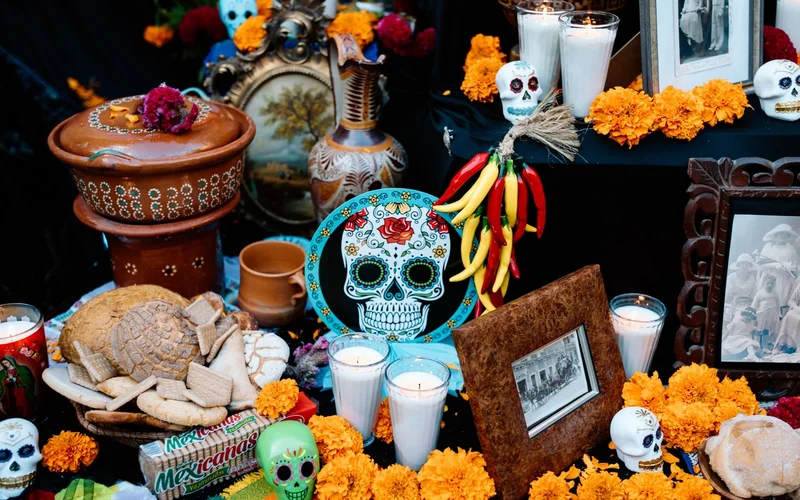 Un altar de Día de Muertos con calaveras de azúcar, pan de muerto, velas, cempasúchil y chiles.