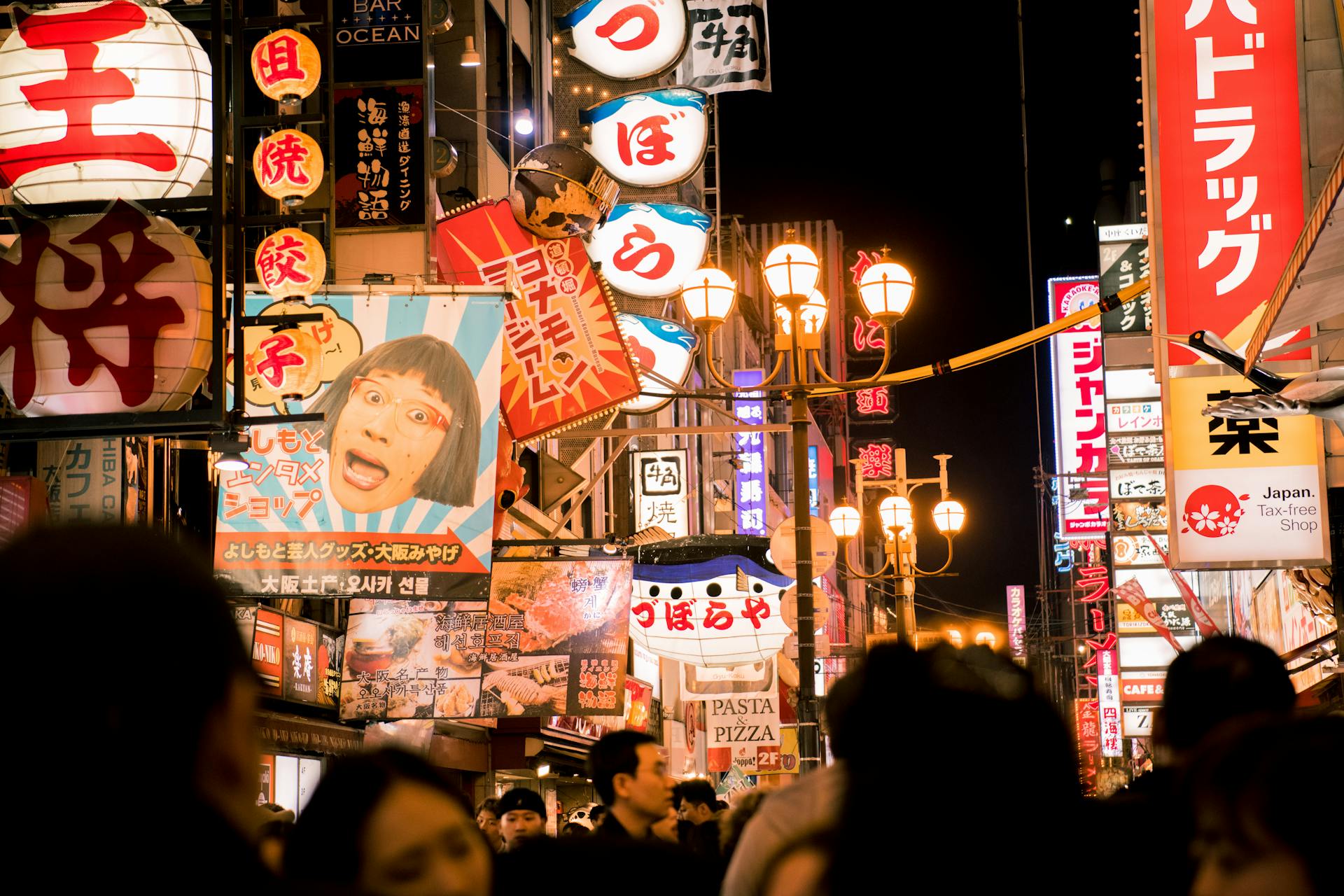 Calle nocturna en Osaka con neones vibrantes, carteles en japonés y multitudes caminando bajo farolas iluminadas