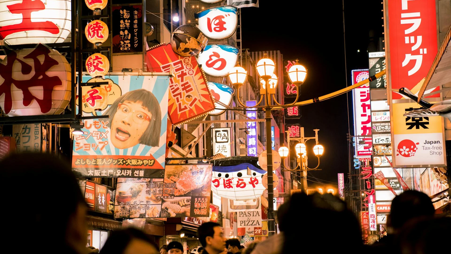 Vista nocturna de una calle animada en Osaka con neones rojos, carteles en japonés y peatones