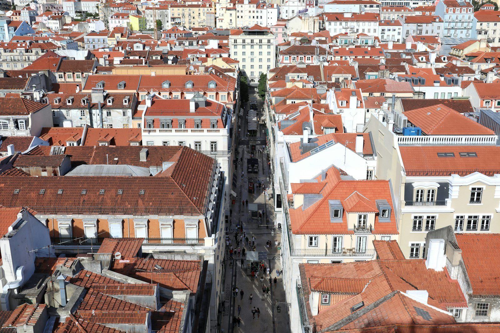 Vista aérea de los tejados rojos y edificios blancos de Lisboa, con una calle central animada por peatones