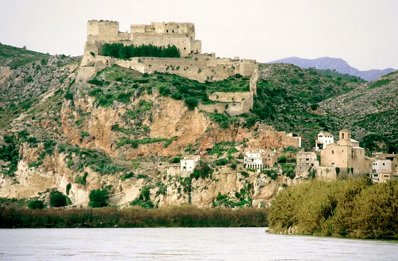 Vista panorámica de un castillo templario en lo alto de un acantilado rocoso junto a un río.