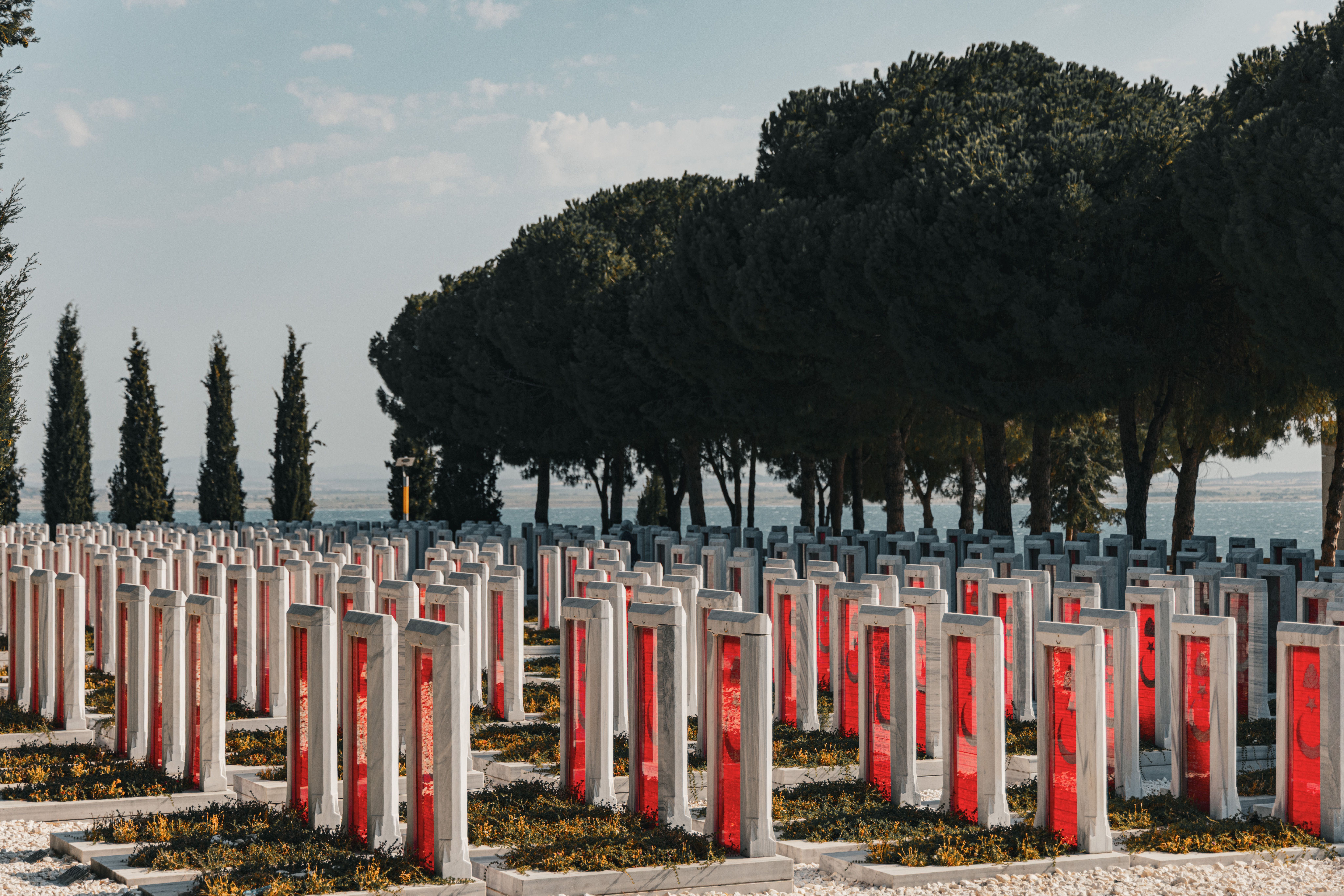Hileras de lápidas modernas de mármol blanco con inserciones rojas en un cementerio junto al mar.