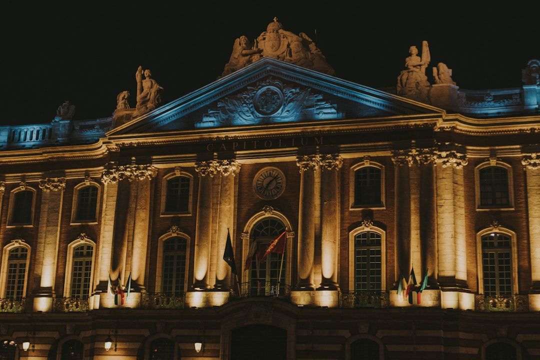 Fachada del Capitolio de Toulouse iluminada en tonos azules y dorados por la noche, con esculturas y banderas en la parte superior