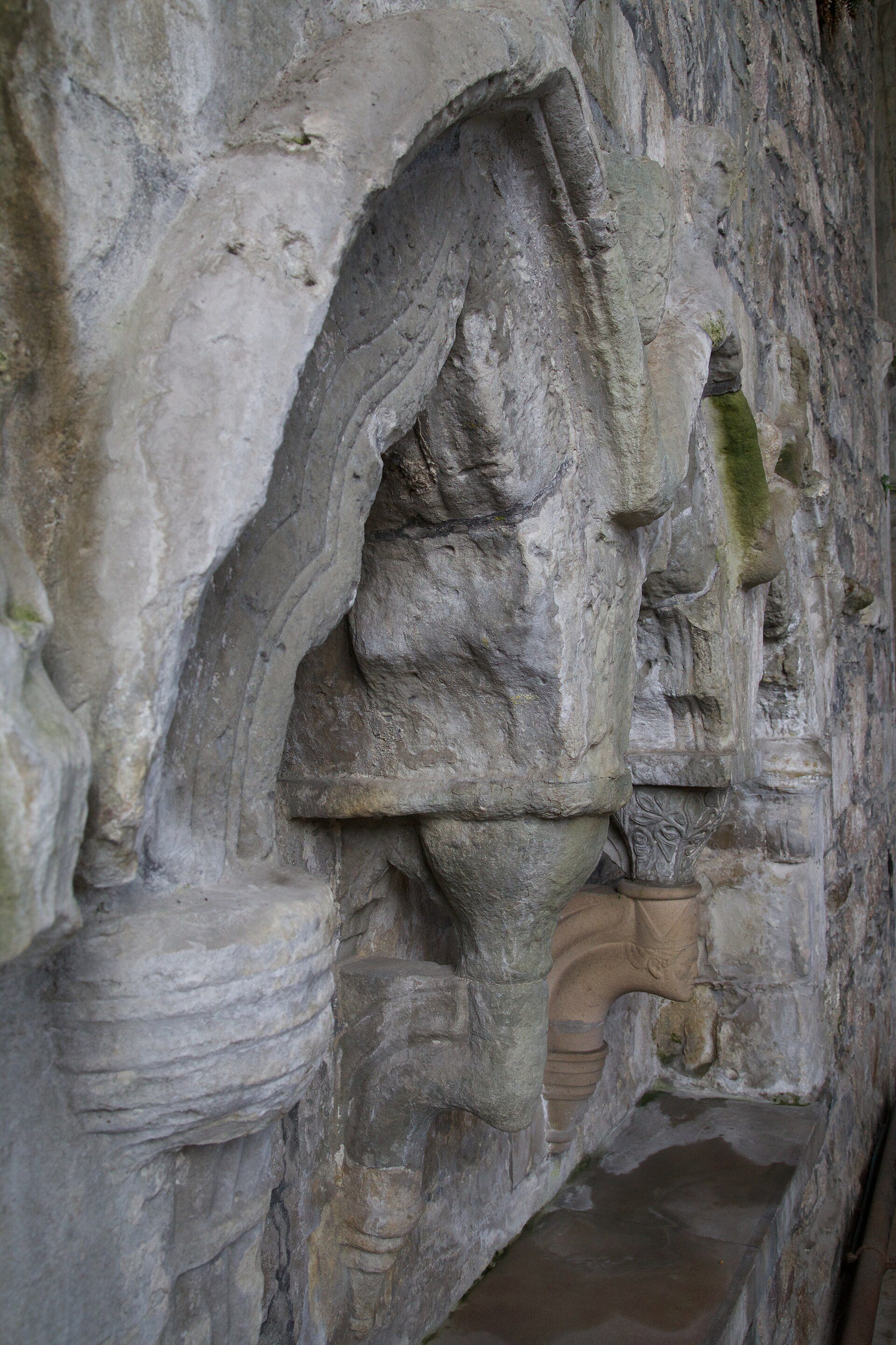 Detalle de una arcada de piedra antigua con relieves y vegetación, mostrando texturas y formas arquitectónicas.