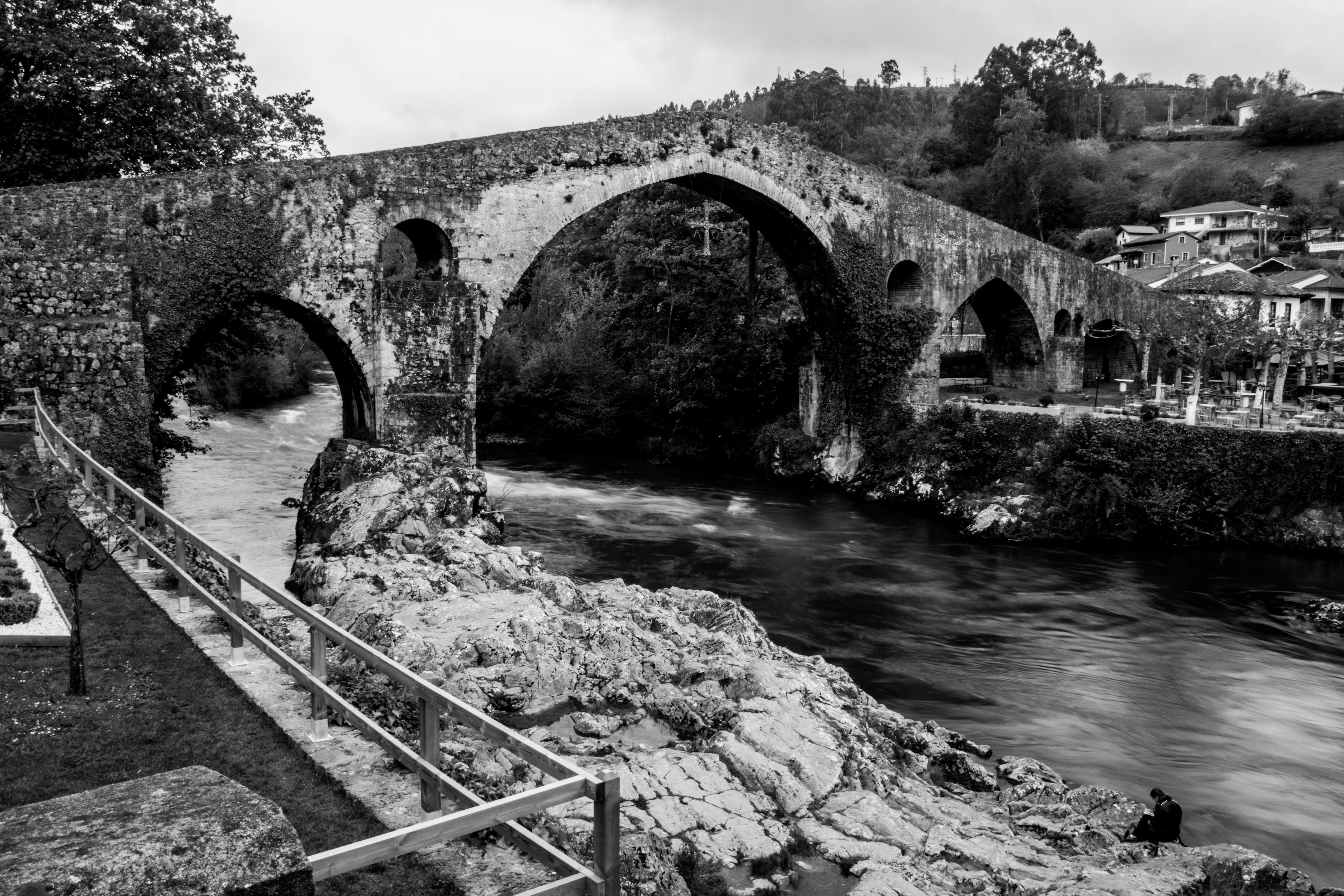 Puente medieval de piedra con arcos sobre un río rocoso, en blanco y negro.