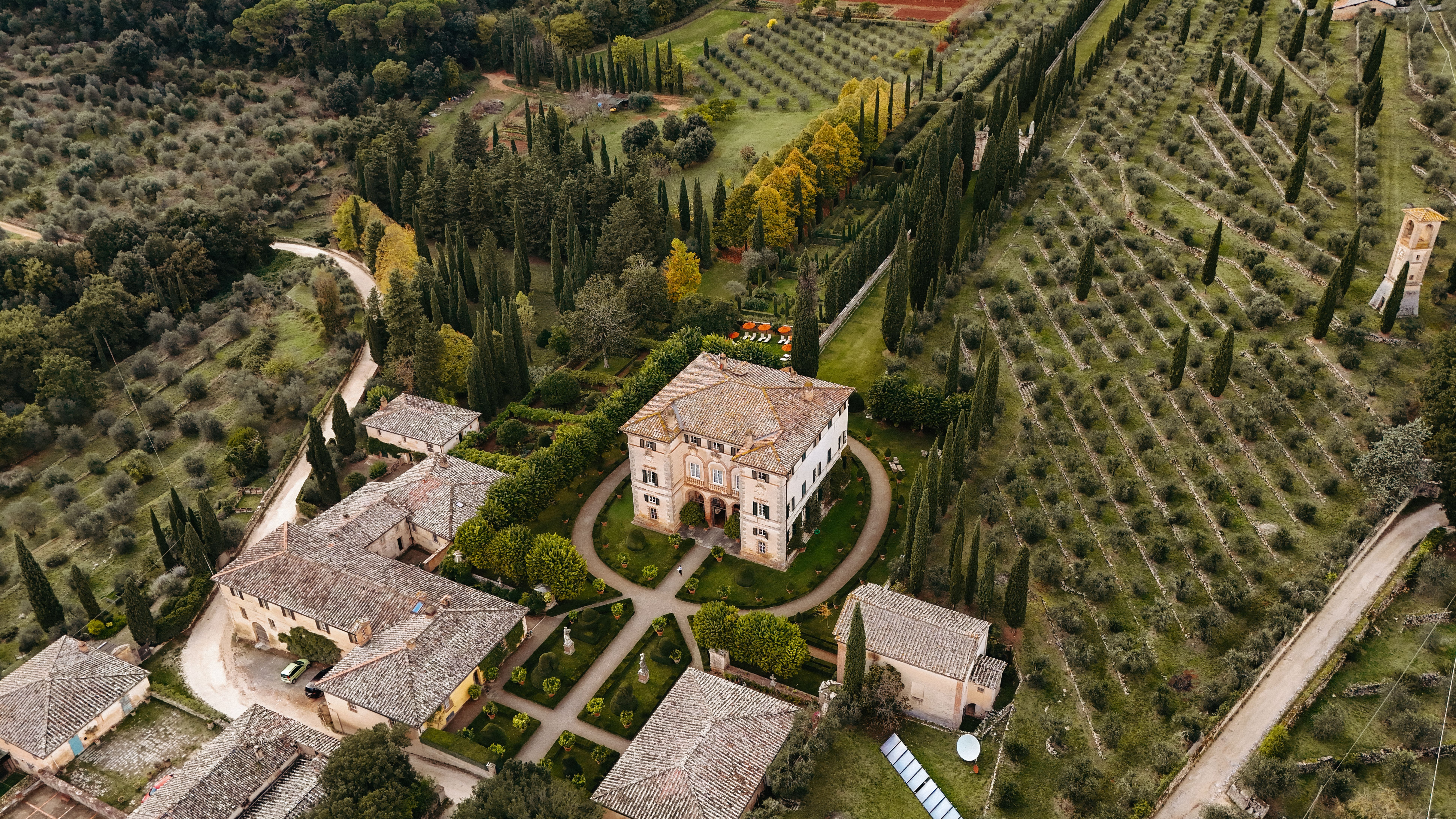 Vista aérea de una finca con edificios históricos, jardines formales y extensos viñedos en la Toscana.