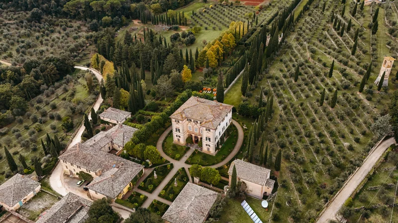 Vista aérea de una finca con edificios históricos, jardines formales y extensos viñedos en la Toscana.