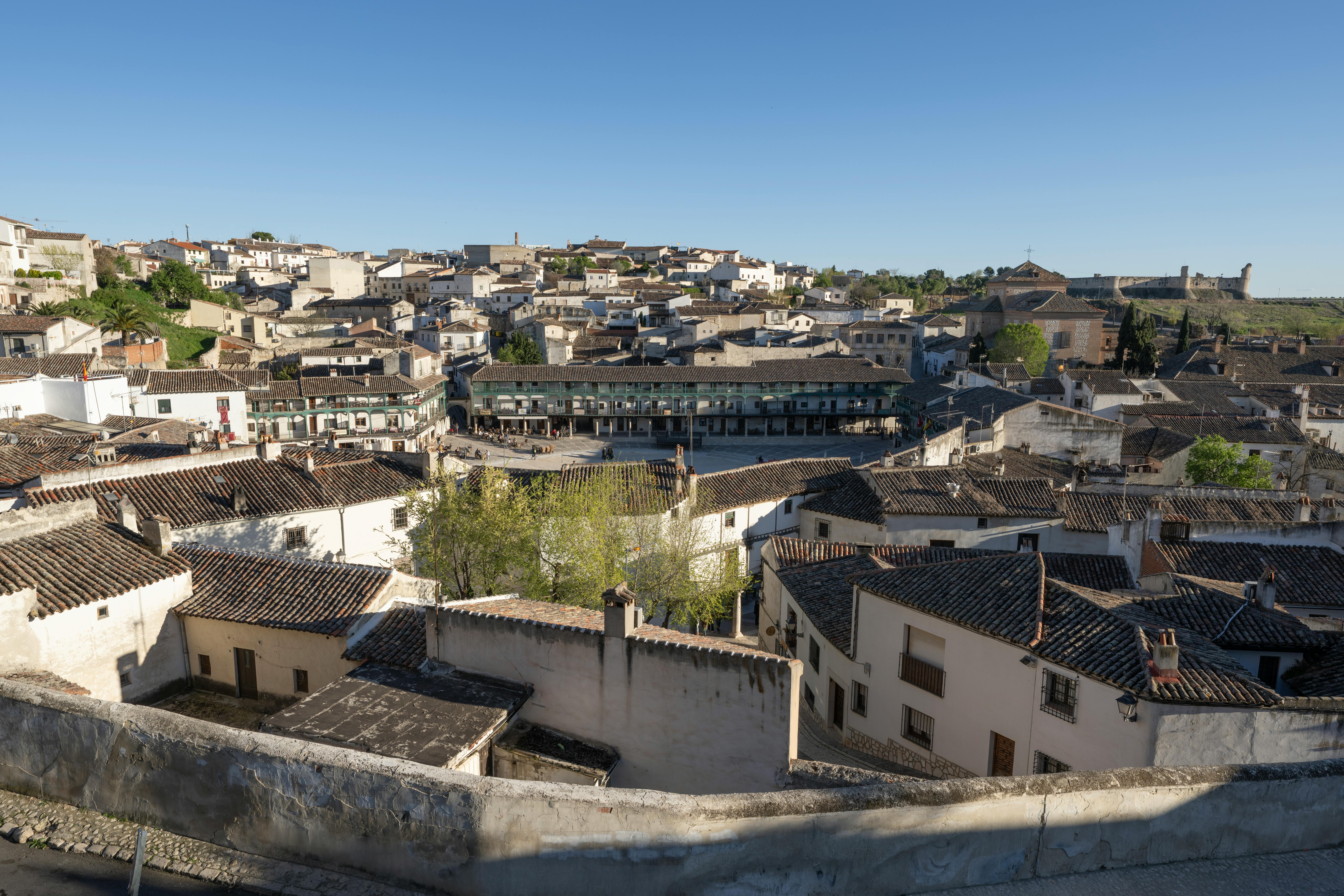 Vista aérea de un pueblo con tejados de teja, edificios blancos y una plaza porticada central.