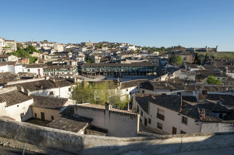 Vista aérea de un pueblo con tejados de teja, edificios blancos y una plaza porticada central.