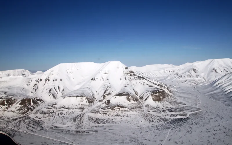 Paisaje nevado de Svalbard con montañas blancas y picos escarpados bajo un cielo azul claro