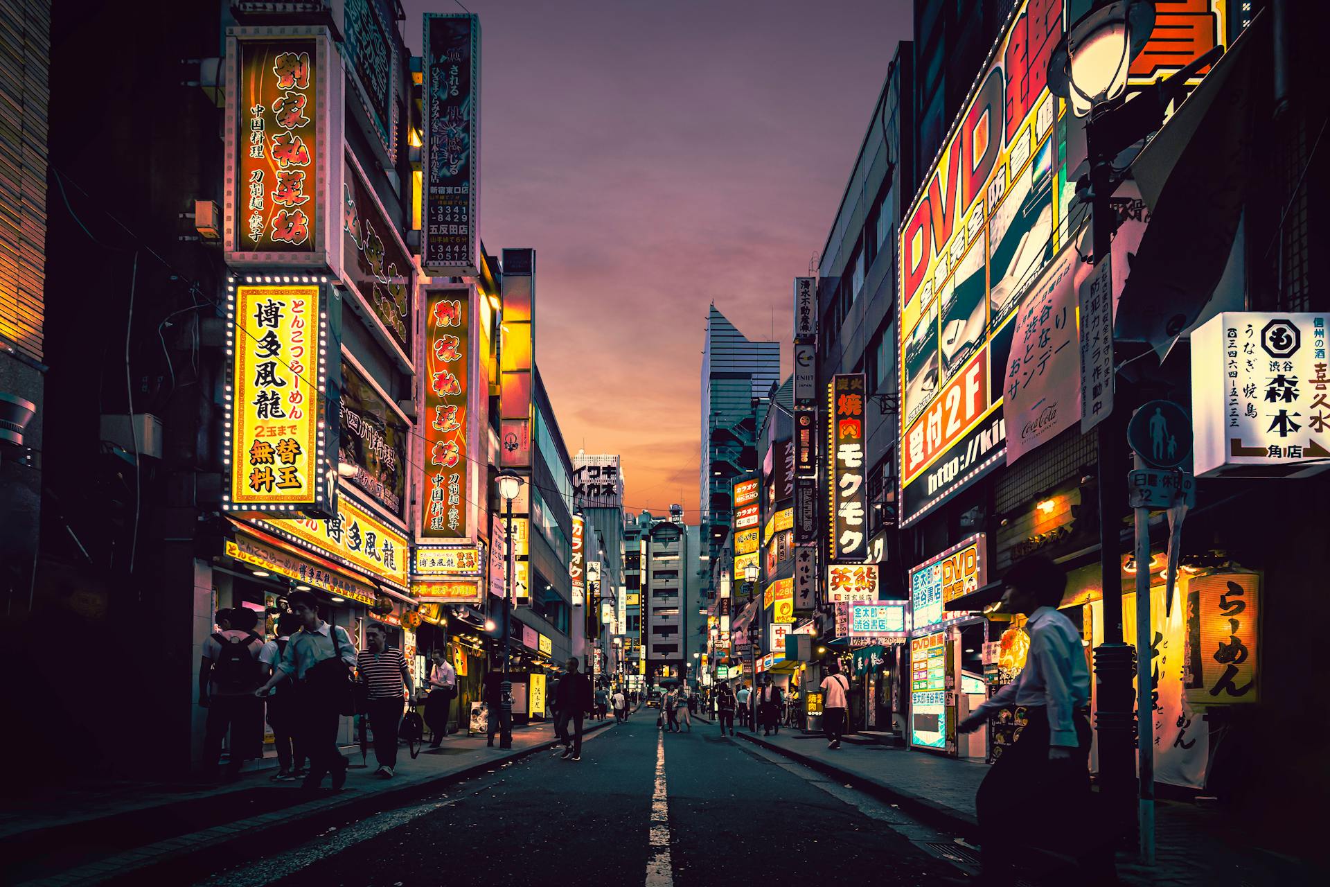 Calle animada en Tokio al atardecer, con neones en japonés de colores vibrantes en edificios altos y peatones cruzando la vía