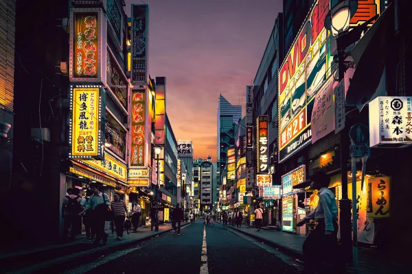 Vista de una calle vibrante en Tokio al atardecer, con neones y letreros en japonés iluminando fachadas, peatones caminando