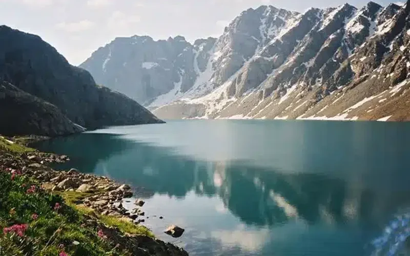 Lago Issyk-Kul de aguas turquesas rodeado de montañas nevadas de Tian Shan y flores silvestres en la orilla