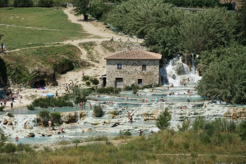 Vista aérea de personas bañándose en cascadas de agua termal azul turquesa junto a un edificio de piedra.