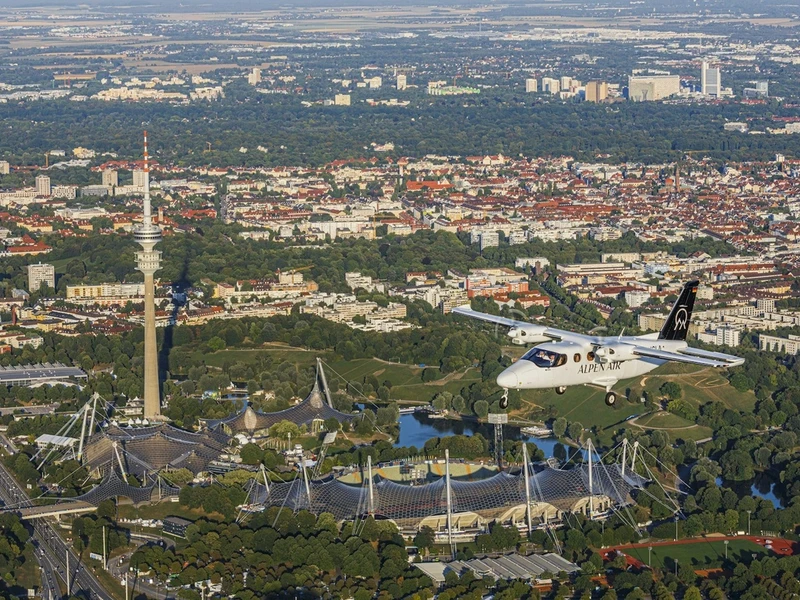 Vista aérea de Múnich con el Allianz Arena, el Olympiapark, la torre de televisión, un avión blanco volando y edificios rodeados de parques y lagos