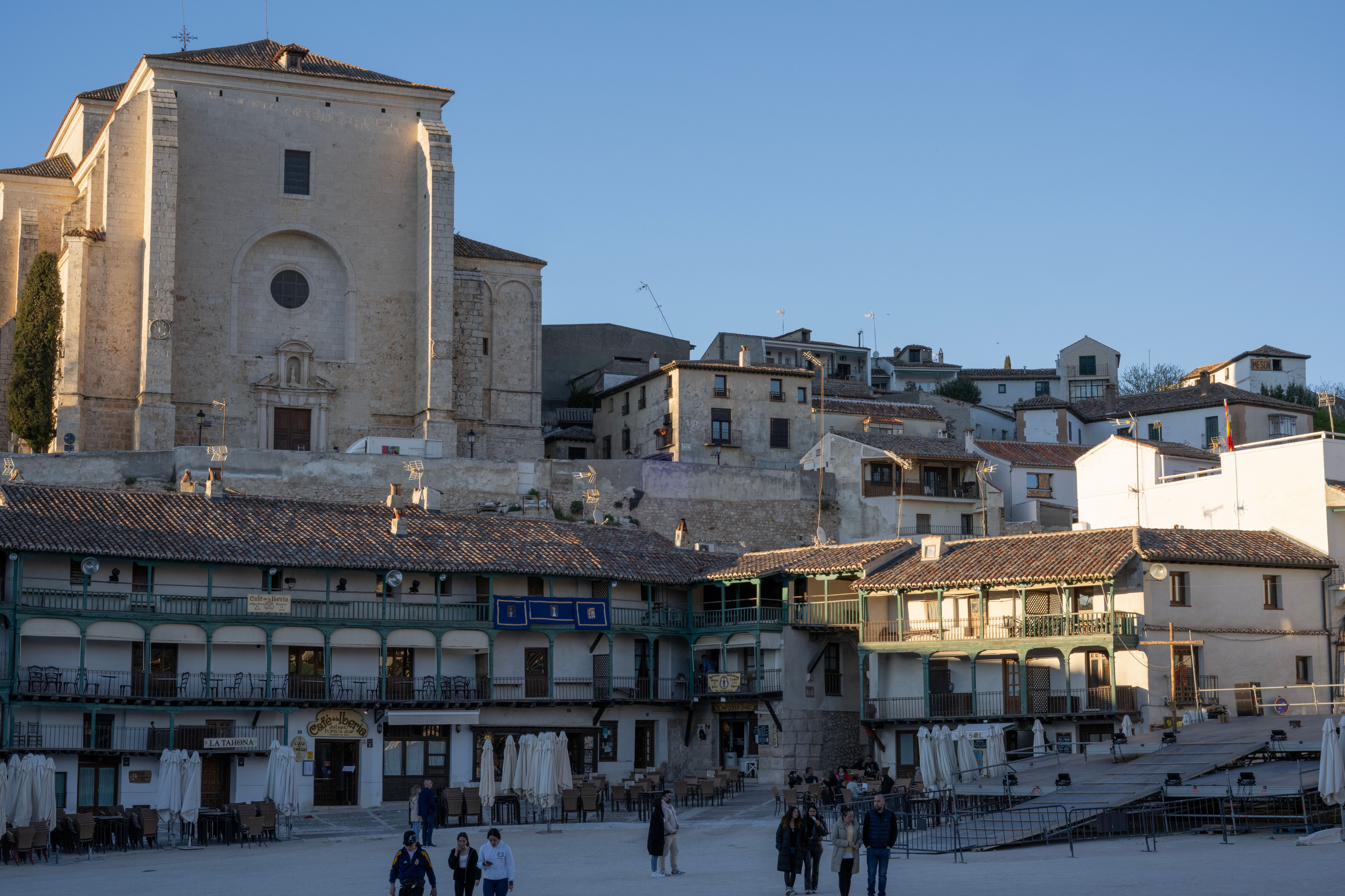 Plaza mayor de Chinchón con edificios históricos y una iglesia al fondo bajo un cielo azul.