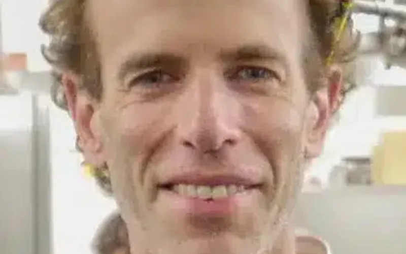 Dan Barber, chef con cabello rojizo y sonrisa, vistiendo chaqueta blanca en una cocina profesional con equipo de acero inoxidable