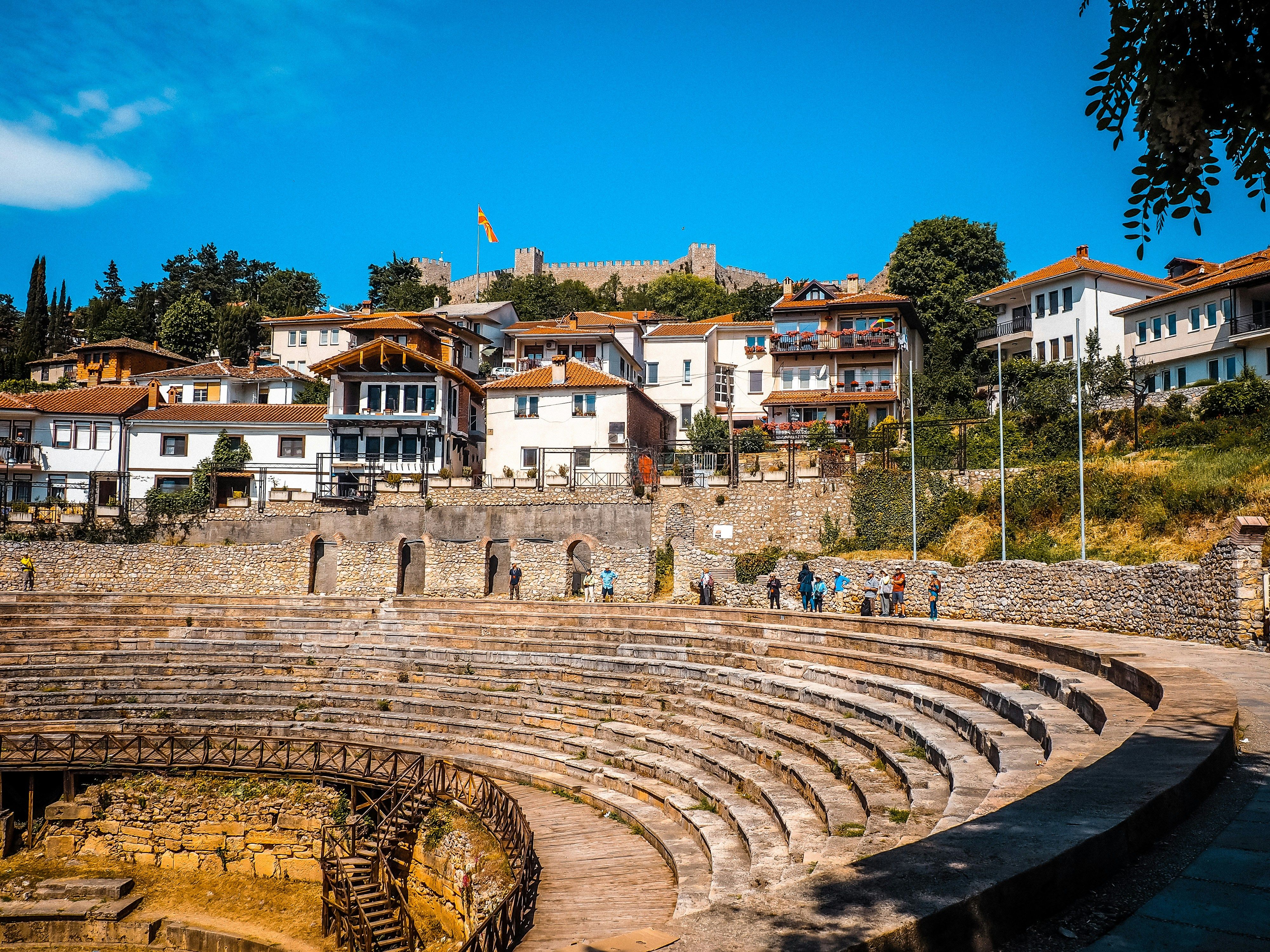 Vista panorámica de un antiguo anfiteatro de piedra con casas y una fortaleza en la colina al fondo.