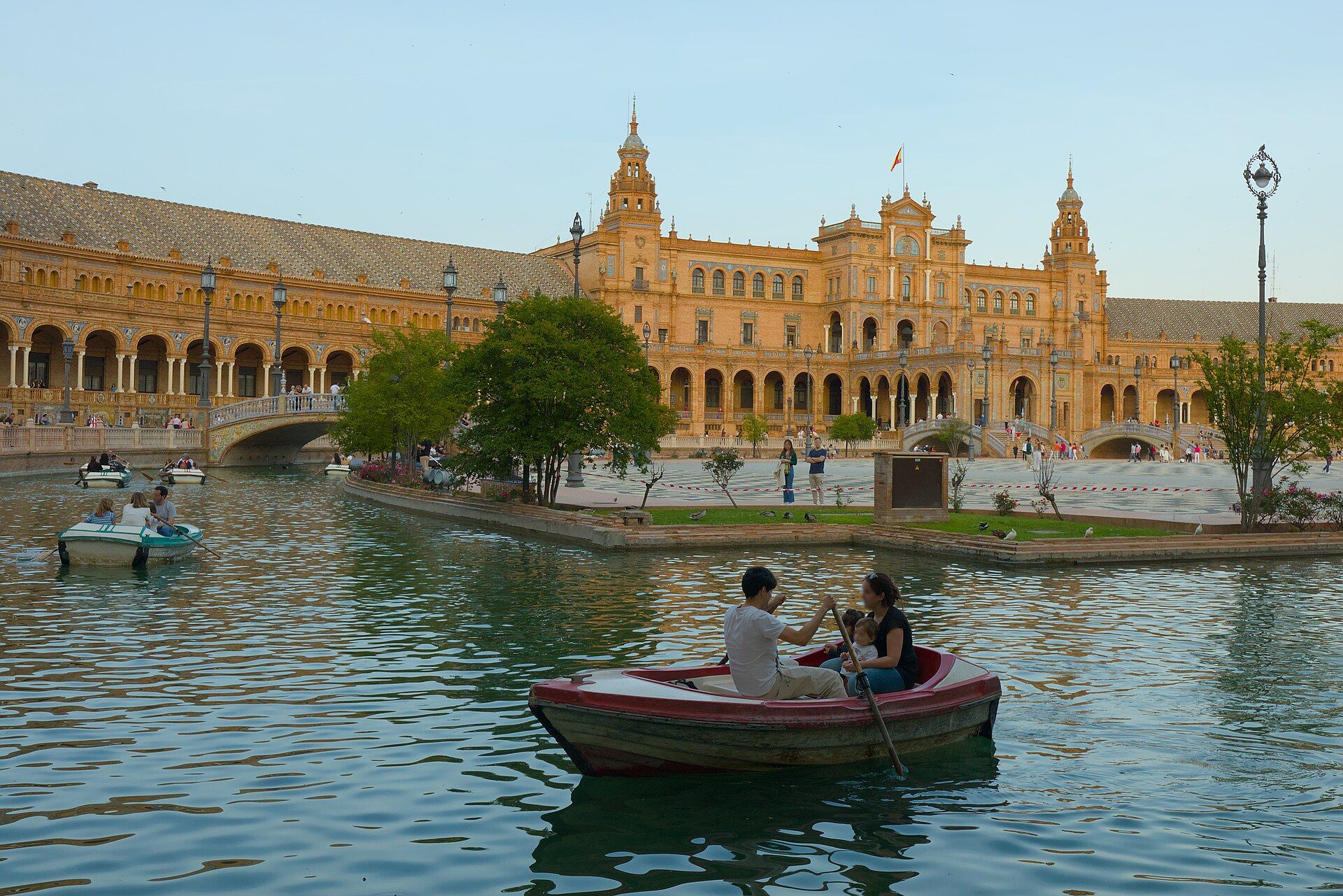 Vista panorámica de la Plaza de España en Sevilla con personas remando en botes por el canal.