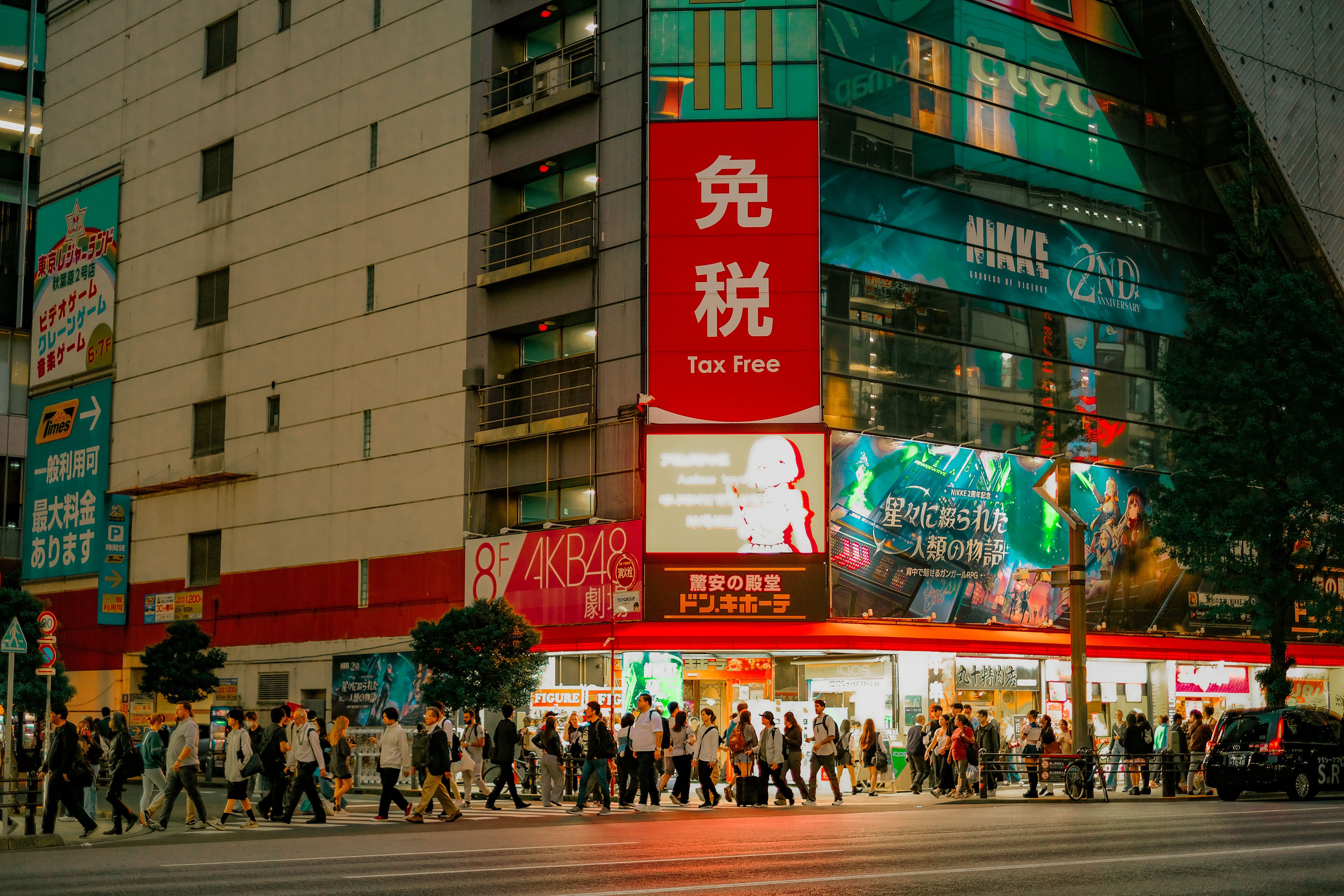 Vista nocturna de un cruce peatonal con gente cruzando frente a edificios comerciales iluminados en Japón.