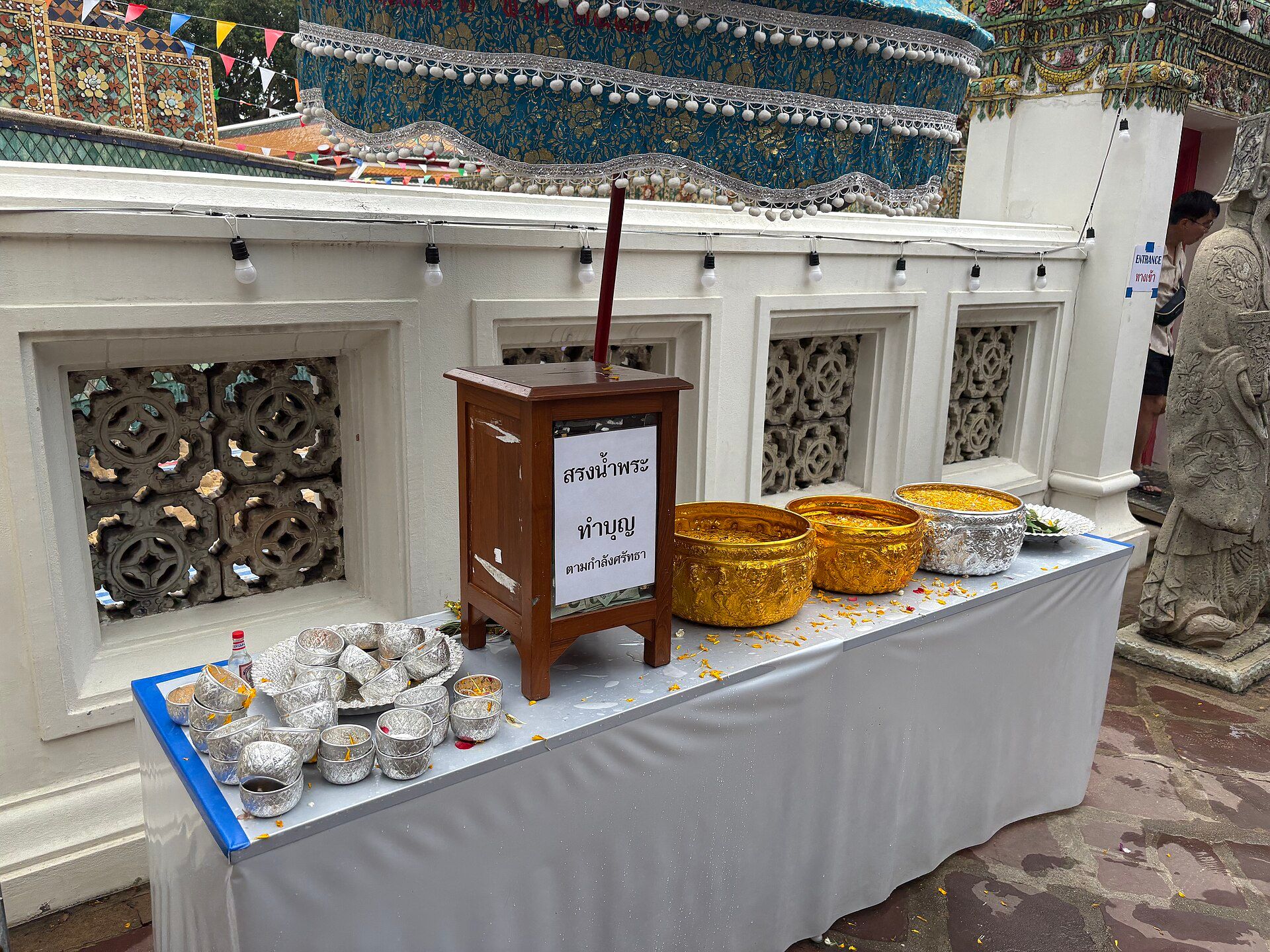 Una mesa con cuencos de metal plateados y dorados, y un cartel con texto tailandés en un templo.