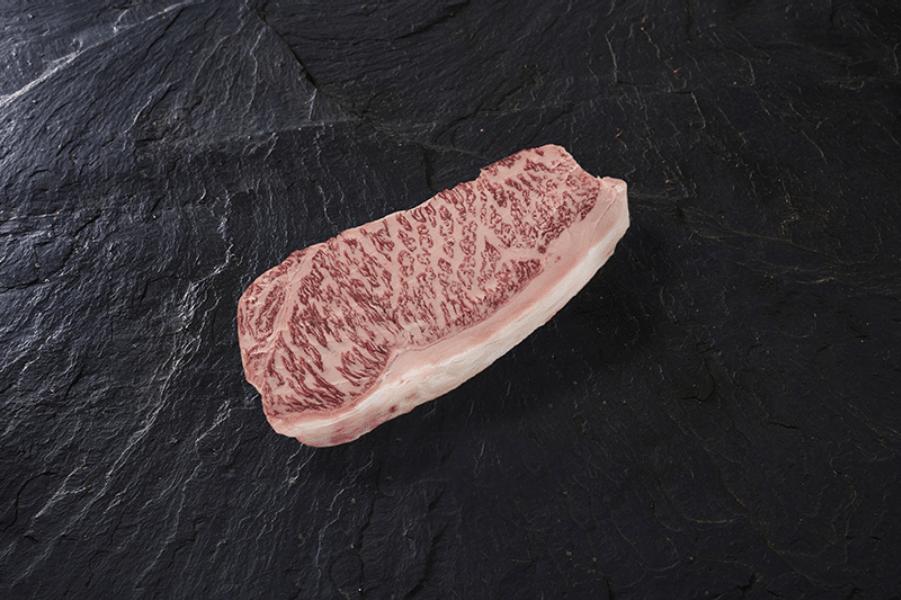 Trozo de carne roja con vetas blancas de grasa marmoleada, sobre una placa de pizarra negra