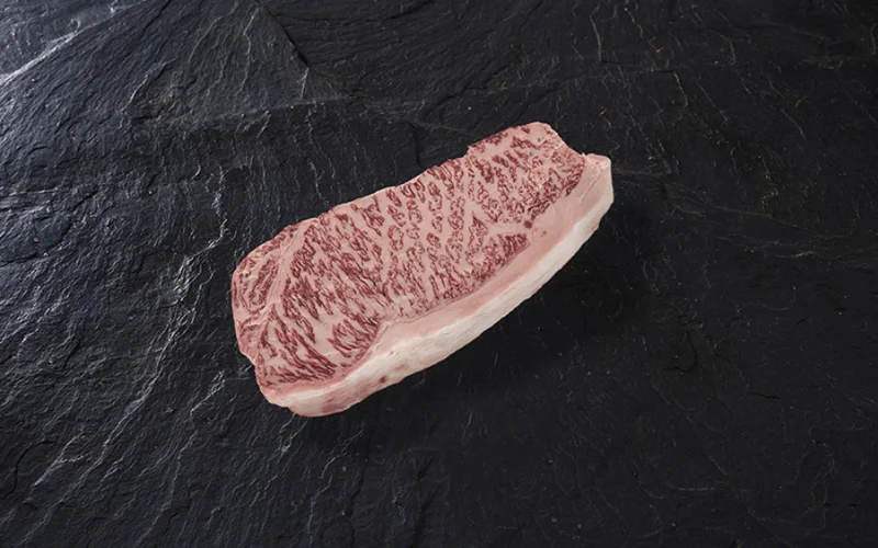Trozo de carne roja con vetas blancas de grasa marmoleada, sobre una placa de pizarra negra