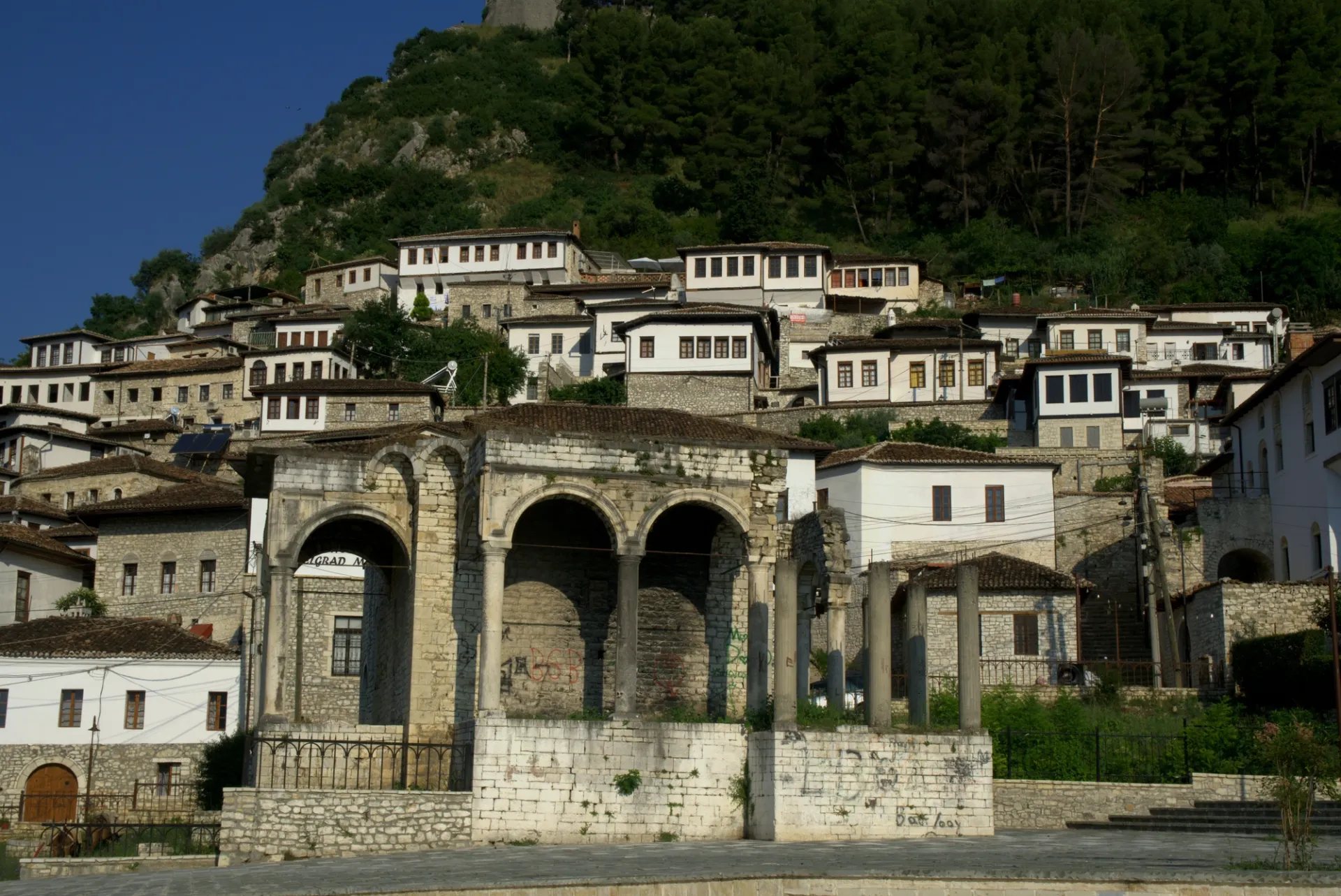 Vista panorámica de casas blancas con tejados oscuros en una ladera, con ruinas de piedra en primer plano.
