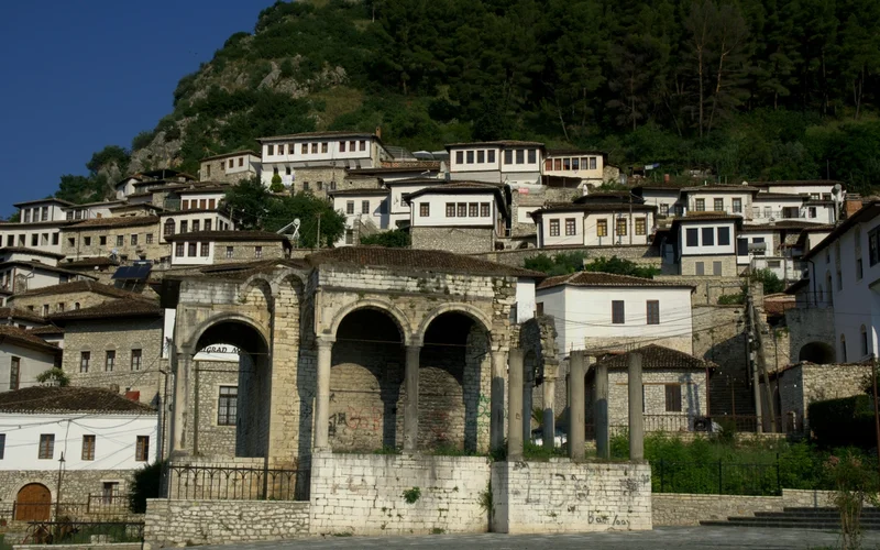 Vista panorámica de casas blancas con tejados oscuros en una ladera, con ruinas de piedra en primer plano.