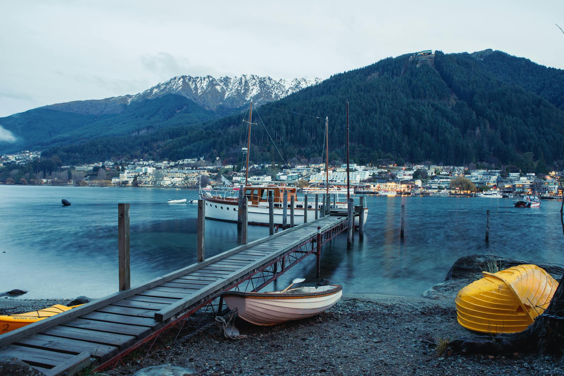 Panorama de Queenstown con lago azul, muelle de madera, barcos amarrados y montañas nevadas al fondo