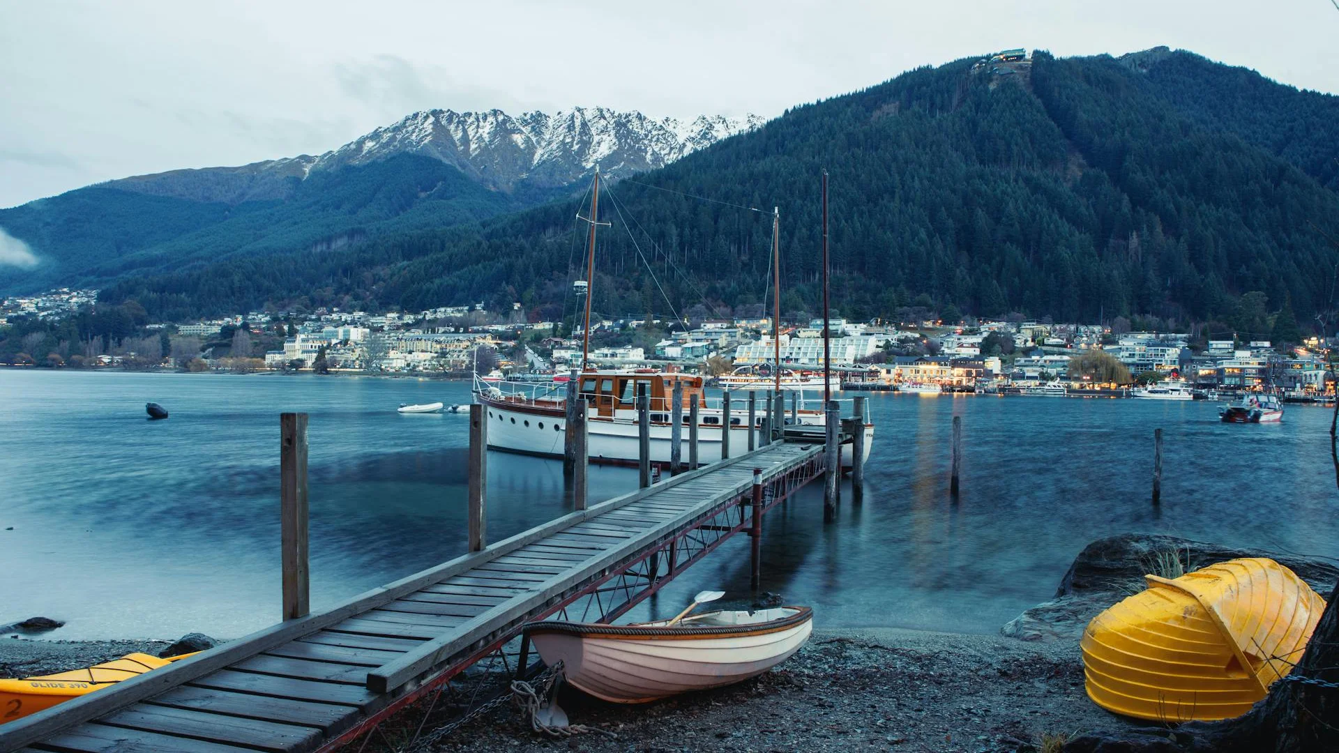 Vista del lago en Queenstown con muelle de madera, botes y montañas nevadas al fondo