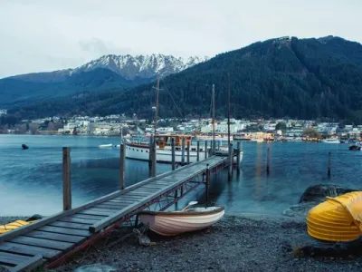 Panorama de Queenstown con lago azul, muelle de madera, barcos amarrados y montañas nevadas al fondo