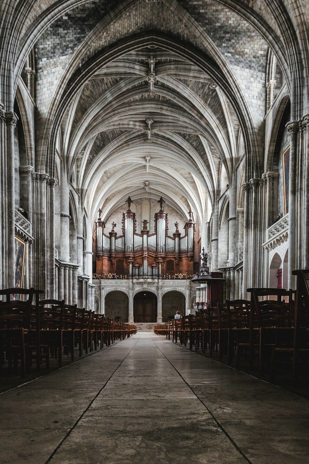 Interior de catedral gótica con altos arcos de piedra, órgano rojo prominente al fondo y filas de bancos de madera