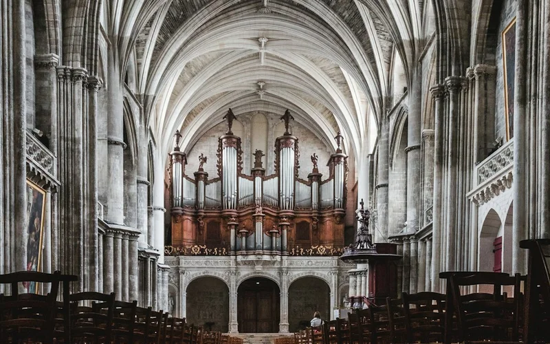 Interior de catedral gótica con altos arcos de piedra, órgano rojo prominente al fondo y filas de bancos de madera