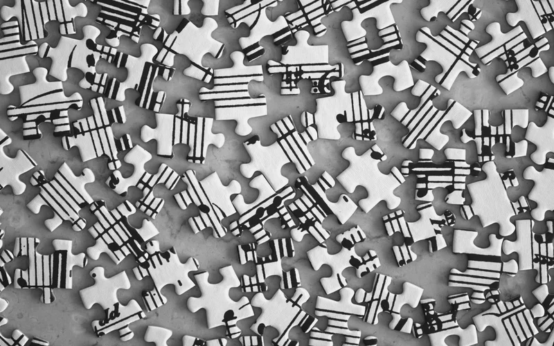 Piezas de rompecabezas blancas y negras dispersas, cada una con fragmentos de partituras musicales.