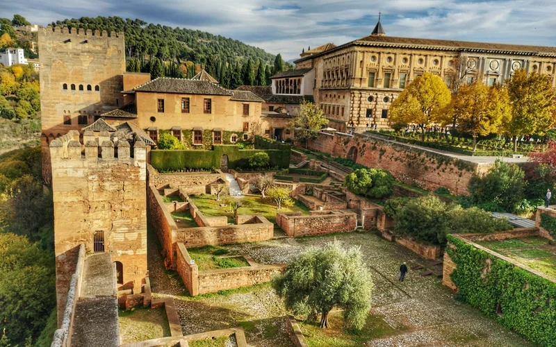 Vista aérea de la Alhambra de Granada con sus jardines, edificios históricos y montañas al fondo.